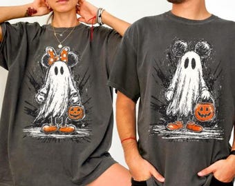 May include: Two charcoal gray t-shirts featuring graphic prints of ghost characters. One ghost wears a polka-dot bow, and both hold orange jack-o'-lantern buckets. The designs are rendered in a distressed white, black, and orange ink style.