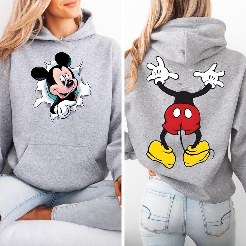 May include: A gray hooded sweatshirt featuring a Mickey Mouse graphic. The front shows Mickey breaking through a torn hole, while the back displays Mickey's body with arms raised. The design includes black, red, yellow, and white colors.