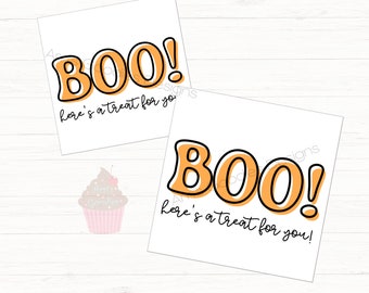 Può includere: Due biglietti quadrati bianchi con la parola "BOO!" in lettere arancioni con un contorno nero. Sotto la parola c'è la frase "here's a treat for you!" in scrittura nera. Una grafica di cupcake rosa si trova nell'angolo in basso a sinistra.