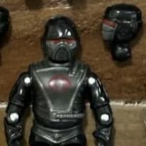 以下が含まれることがあります： 赤いバイザー付きのヘルメット、赤いエンブレム付きの胸部プレート、関節を備えた、未来的な兵士の黒いアクションフィギュア。フィギュアは、グレーのアクセントが付いた黒いユニフォームを着ています。別のヘルメットパーツも表示されています。