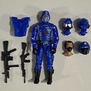 Può includere: Una action figure blu con un casco nero e un simbolo Cobra rosso sul petto. La figura viene fornita con due pistole nere, un pezzo per il petto blu, un casco blu, una maschera facciale blu e una testa blu.