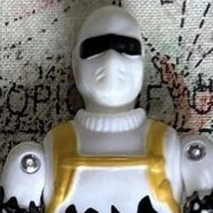 May include: White action figure with a black mask and gold accents. The figure is wearing a white jumpsuit with a black design.