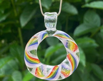 May include: A clear glass pendant with a rainbow swirl design. The pendant is circular with a hole in the center and hangs from a silver chain. The rainbow colors include red, orange, yellow, green, blue, and purple.