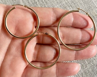 Puede incluir: Tres pendientes de aro de oro de diferentes tamaños. Los pendientes son lisos y tienen un acabado brillante.