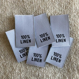 May include: Six white fabric labels with black text reading "100% LINEN" on each label.