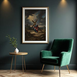 Op de afbeelding: Een ingelijste prent toont een figuur die een kruis draagt over een rotsachtig terrein onder een dramatische lucht. Het kunstwerk gebruikt blauw, rood en bruin, en is geplaatst in een gouden lijst. De prent hangt aan een donkerblauwe muur.