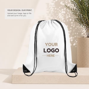 May include: A white drawstring backpack with black drawstrings and reinforced corners. The bag features the text "YOUR LOGO HERE" in brown and a tagline. The text "YOUR DESIGN. OUR PRINT. Upload your image, logo or file and we'll print it for you." is also visible.