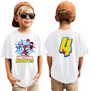Puede incluir: Camiseta blanca con dise&ntilde;o de Spider-Man. La parte delantera muestra una telara&ntilde;a azul con Spider-Man y otros personajes, junto con el texto "MICHAEL BIRTHDAY BOY". La parte trasera muestra el n&uacute;mero 4 con Spider-Man. La camiseta la lleva un ni&ntilde;o.