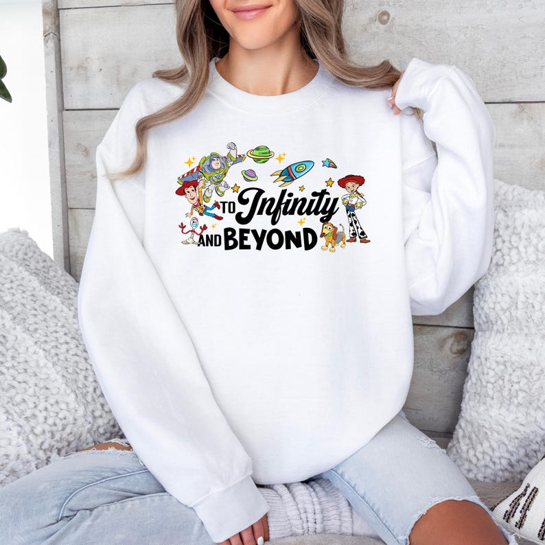 Unisex white sweatshirt featuring a colorful Toy Story design with Woody, Buzz Lightyear, Jessie, Forky, and Slinky Dog around the phrase “To Infinity and Beyond.” Cozy Disney-inspired crewneck sweater, perfect for Pixar fans and casual everyday wear.