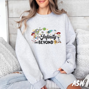 Puede incluir: Una sudadera gris con un estampado gr&aacute;fico de personajes de la franquicia de pel&iacute;culas Toy Story. El gr&aacute;fico incluye los personajes Woody, Buzz Lightyear y otros personajes de la pel&iacute;cula. El texto "To Infinity and Beyond" est&aacute; impreso en la sudadera.