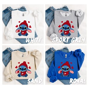 Peut inclure: Quatre sweat-shirts de couleurs diff&eacute;rentes avec un Stitch de dessin anim&eacute; portant un chapeau rouge et tenant un c&oelig;ur. Les sweat-shirts sont blanc, gris sport, sable et bleu royal.