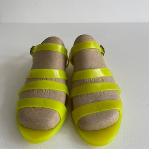 May include: A pair of bright yellow jelly sandals with a buckle fastening. The sandals have a simple design with multiple straps across the foot.