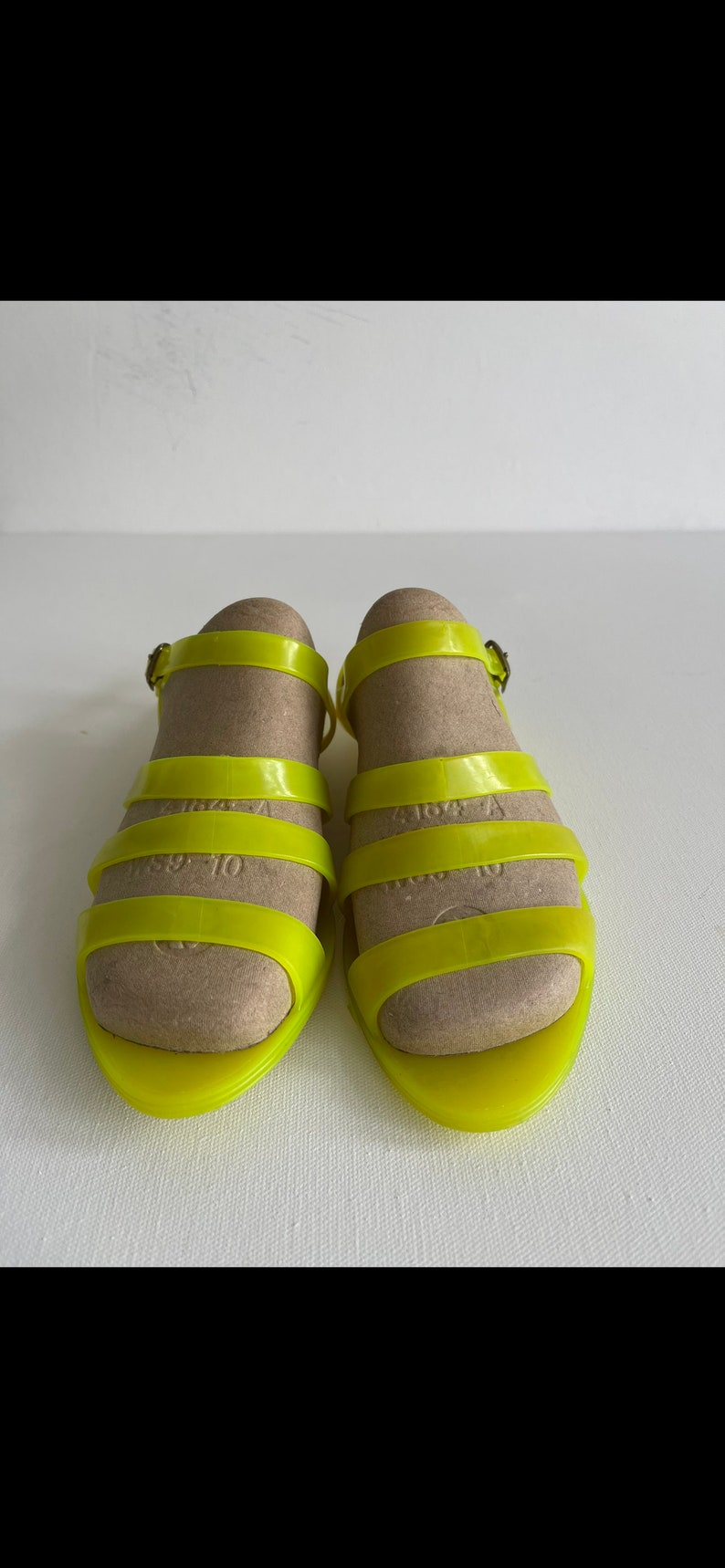 May include: A pair of bright yellow jelly sandals with a buckle fastening. The sandals have a simple design with multiple straps across the foot.
