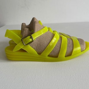 May include: Neon yellow jelly sandals with a buckle fastening and a platform sole.