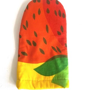 May include: A fabric oven mitt featuring a vibrant pattern of red and orange sections with dark brown teardrop-shaped seeds, accented by a bright yellow base and a large green leaf graphic at the bottom edge, designed for kitchen use.
