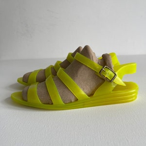 May include: Neon yellow rubber sandals with a buckle fastening and a platform sole.