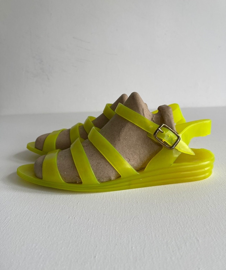 May include: Neon yellow rubber sandals with a buckle fastening and a platform sole.