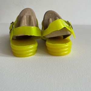 May include: A pair of bright yellow jelly sandals with a buckle fastening. The sandals are made of a translucent material and have a ridged sole.