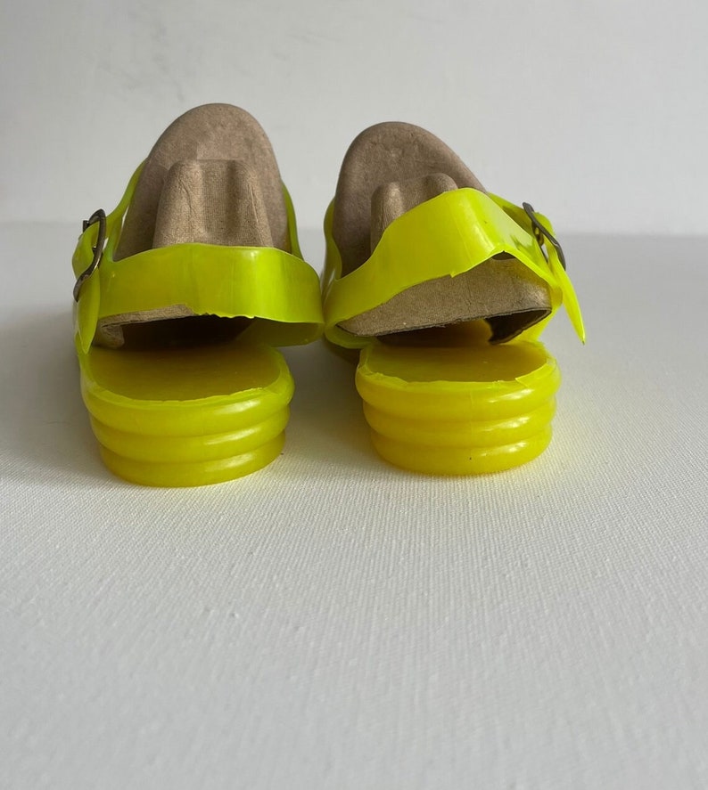 May include: A pair of bright yellow jelly sandals with a buckle fastening. The sandals are made of a translucent material and have a ridged sole.