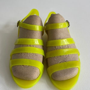 May include: A pair of bright yellow jelly sandals with adjustable ankle straps and buckles. The sandals have a simple design with multiple straps across the foot.