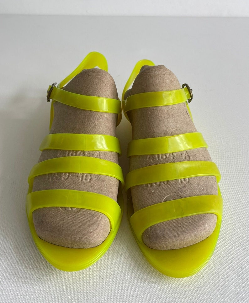 May include: A pair of bright yellow jelly sandals with adjustable ankle straps and buckles. The sandals have a simple design with multiple straps across the foot.