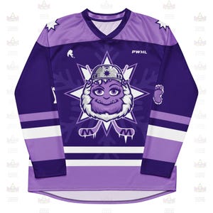 May include: Purple hockey jersey with a V-neck design. The jersey features a cartoon yeti character in the center, set against a white starburst and snowflake pattern. The sleeves have white and purple stripes, and the text "PWHL" is visible.
