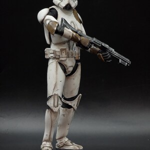 以下が含まれることがあります： スターウォーズのストームトルーパーの風化した白と茶色のフィギュア。ブラスターライフルを持っています。フィギュアは詳細なヘルメット、鎧、ブーツを備えています。フィギュアは暗い背景に立っています。