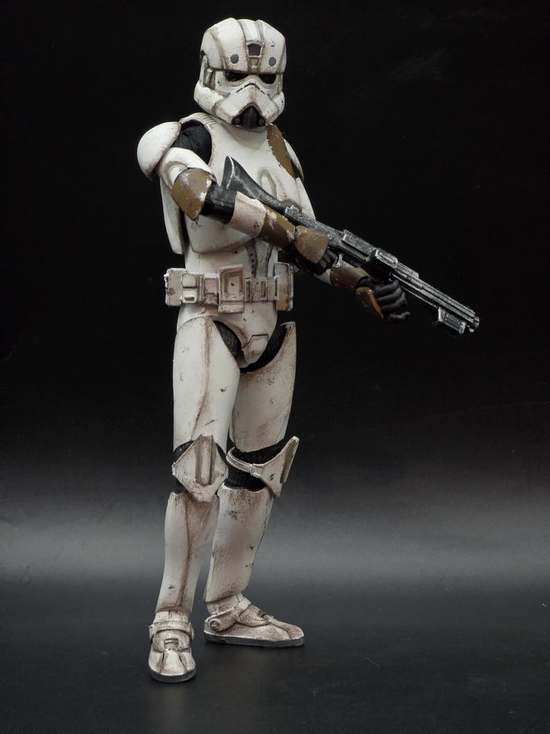 以下が含まれることがあります： スターウォーズのストームトルーパーの風化した白と茶色のフィギュア。ブラスターライフルを持っています。フィギュアは詳細なヘルメット、鎧、ブーツを備えています。フィギュアは暗い背景に立っています。