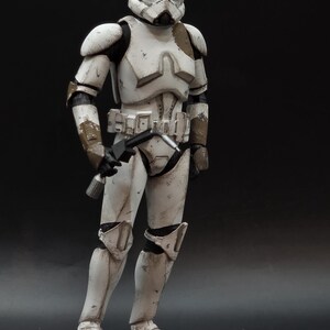 以下が含まれることがあります： 白いと茶色のアーマーを着たストームトルーパーのアクションフィギュア。ブラスターを保持しています。フィギュアは摩耗や損傷が見られ、暗い背景に配置されています。コレクターアイテムです。