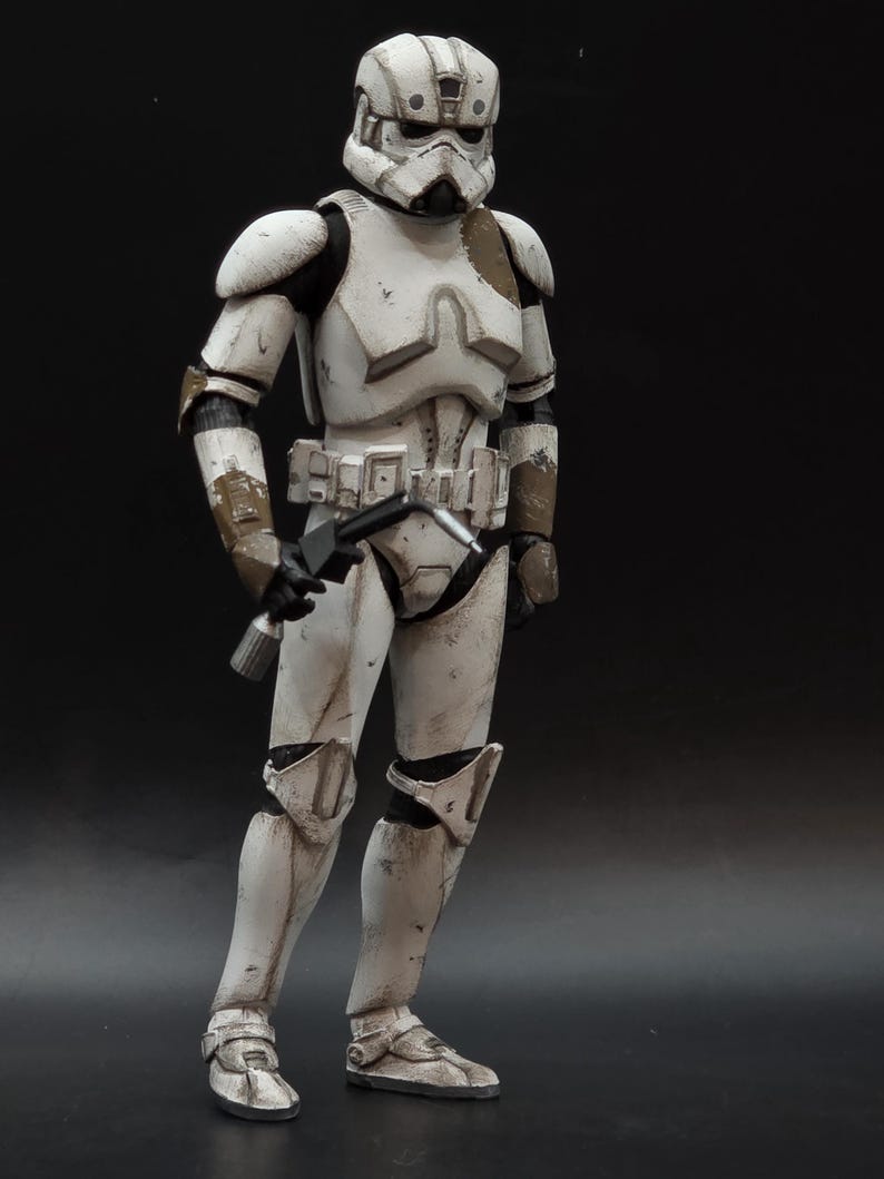 以下が含まれることがあります： 白いと茶色のアーマーを着たストームトルーパーのアクションフィギュア。ブラスターを保持しています。フィギュアは摩耗や損傷が見られ、暗い背景に配置されています。コレクターアイテムです。