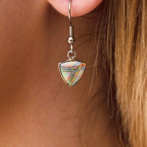 May include: Silver dangle earrings with a triangular iridescent opal gemstone. The opal has a rainbow of colors, including pink, orange, yellow, green, and blue.