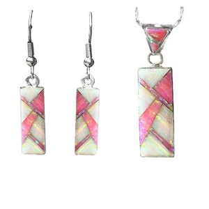 Op de afbeelding: Een sieradenset met oorbellen en een hangerketting. De oorbellen en hanger hebben een rechthoekige vorm met een geometrisch ontwerp van wit, roze en zilverkleurig metaal. De ketting heeft een zilveren ketting.