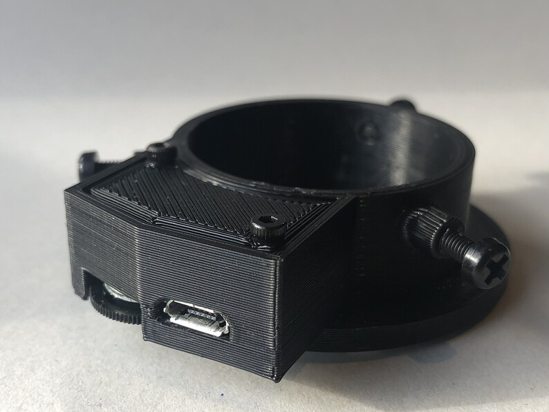 May include: A black 3D printed camera mount with a micro USB port. The mount has a threaded hole on the bottom and a screw on the side.
