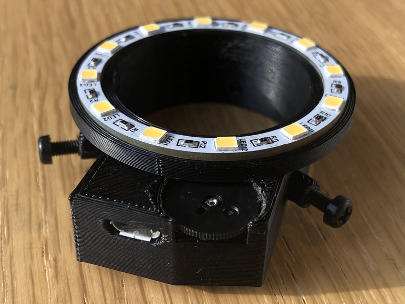 May include: A black 3D printed ring light with a USB port and a knob for adjusting the light. The ring light has 12 white LED lights around the circumference.