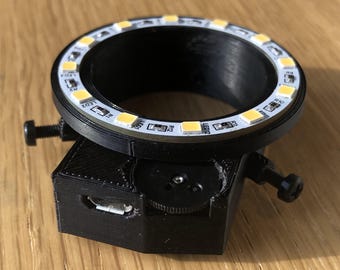 May include: A black 3D printed ring light with a USB port and a knob for adjusting the brightness. The ring light has 18 white LED lights around the circumference.