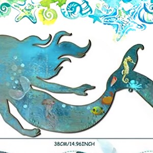 May include: A blue-toned wooden mermaid wall cutout featuring a painted sea life design on the tail, including a seahorse, octopus, and fish. The piece measures 21.5 cm by 38 cm, with a watercolor-style border of shells and starfish.