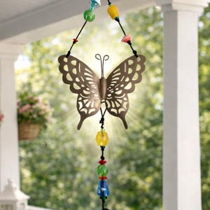 May include: A decorative wind chime featuring a brown metal butterfly with intricate cut-out details. The butterfly hangs from a string adorned with colorful beads and a small bell, perfect for outdoor decor.