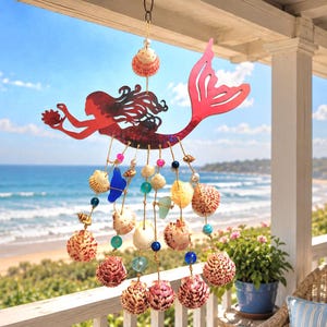 May include: A hanging mobile featuring a red metal mermaid silhouette holding a small shell. Below the mermaid, multiple strands of twine are adorned with various natural seashells, blue sea glass pieces, and colorful glass beads.