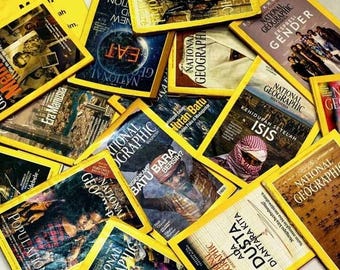 Könnte beinhalten: Nahaufnahme eines Stapels National Geographic Magazine mit gelben Umschlägen. Die Umschläge zeigen verschiedene Bilder und Texte, darunter "Eat", "Gender", "ISIS", "Dust" und "Batu Bara".