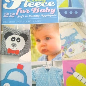 May include: A book titled "Easy Fleece for Baby" with the subtitle "22 Soft & Cuddly Appliqués" is displayed. The image also shows a baby, a panda bear pillow, a blue car, a blue baby outfit, and a cat applique.