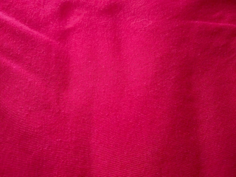 May include: Close-up of a vibrant, solid magenta fabric. The textile has a slightly textured appearance with subtle diagonal lines, creating a sense of depth and visual interest. The color is rich and saturated.