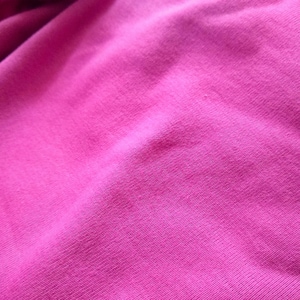 May include: Close-up of a vibrant fuchsia fabric, showcasing the texture and folds of the material. The image highlights the rich color and the subtle variations in the knit, suggesting a soft and comfortable textile.