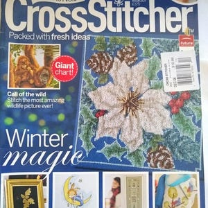 May include: A magazine cover for "Cross Stitcher" features a large cross-stitch design of a flower and pinecones. The cover includes text such as "Winter Magic" and "Call of the Wild". Additional small images showcase cross-stitch projects.