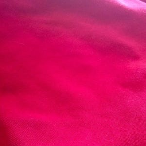 May include: A close-up shot of a vibrant, fuchsia-colored fabric. The material has a soft, slightly textured appearance, with subtle variations in tone creating depth. The fabric is smooth and appears to be draped, with gentle folds and shadows.