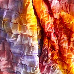 Może przedstawiać: Zbliżenie na tkaninę z wzorem tie-dye w odcieniach fioletu, pomarańczy i ż&oacute;łci. Tkanina jest fakturowana i ma pomarszczony wygląd.