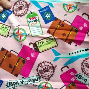 May include: Pink fabric with a repeating pattern of suitcases, airplanes, paw prints, and the text "First Class Dog Priority", "Top Priority Kitten", "Bon Voyage!" and "Millie's Widdly Island, WA".