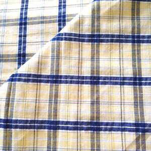 Puede incluir: Una tela de cuadros amarilla y azul con un pliegue diagonal. La tela tiene una textura tejida.