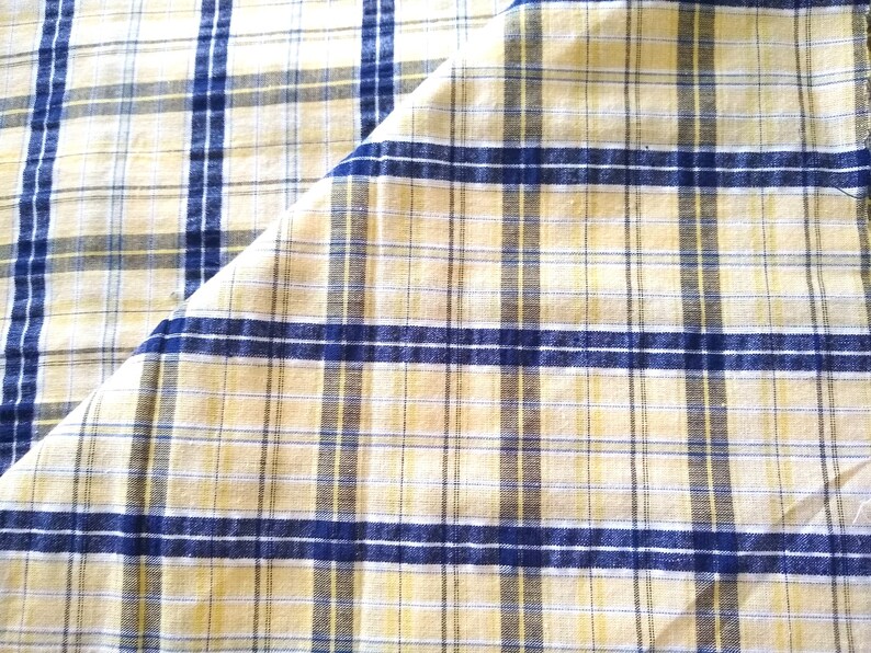 Puede incluir: Una tela de cuadros amarilla y azul con un pliegue diagonal. La tela tiene una textura tejida.