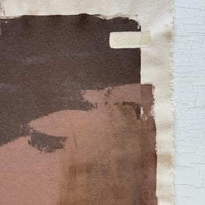 May include: Abstract artwork on canvas featuring a palette of brown, tan, and blush tones. The composition includes broad brushstrokes and a raw canvas edge, creating a textured, artistic aesthetic. The artwork is mounted on a white surface.