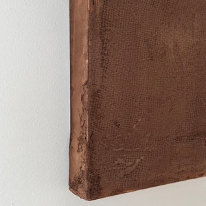 May include: Close-up of the edge of a brown canvas painting. The canvas has a textured surface and is stretched over a wooden frame.